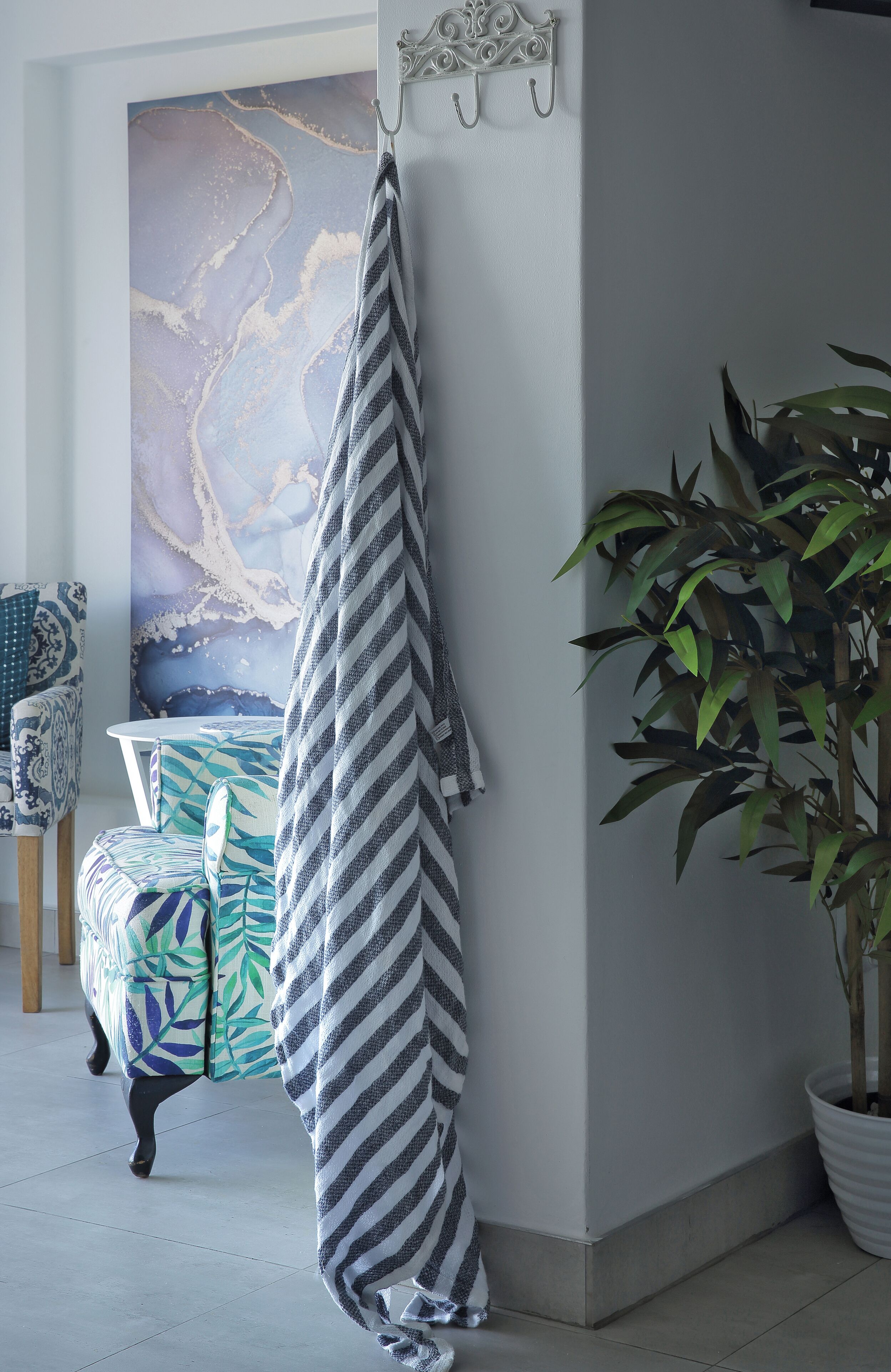 A room with a large abstract painting, a striped towel hanging on a hook, a patterned chair, and a potted plant.