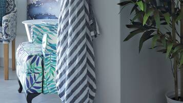 A room with a large abstract painting, a striped towel hanging on a hook, a patterned chair, and a potted plant.
