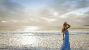 A person in a blue dress standing on a beach with waves.