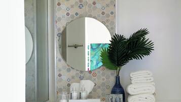 Une salle de bain avec un lavabo blanc, un miroir, un vase bleu contenant une plante et une pile de serviettes blanches.
