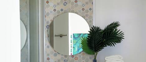 A bathroom with a white sink, a mirror, a blue vase with a plant, and a stack of white towels.