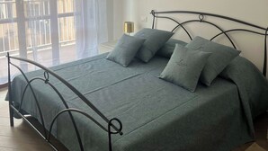 A bedroom with a metal bed frame, grey bedding, and an air conditioning unit on the wall.