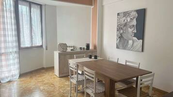 Un'area pranzo con un tavolo e sedie in legno, un quadro appeso al muro e una finestra con tende.