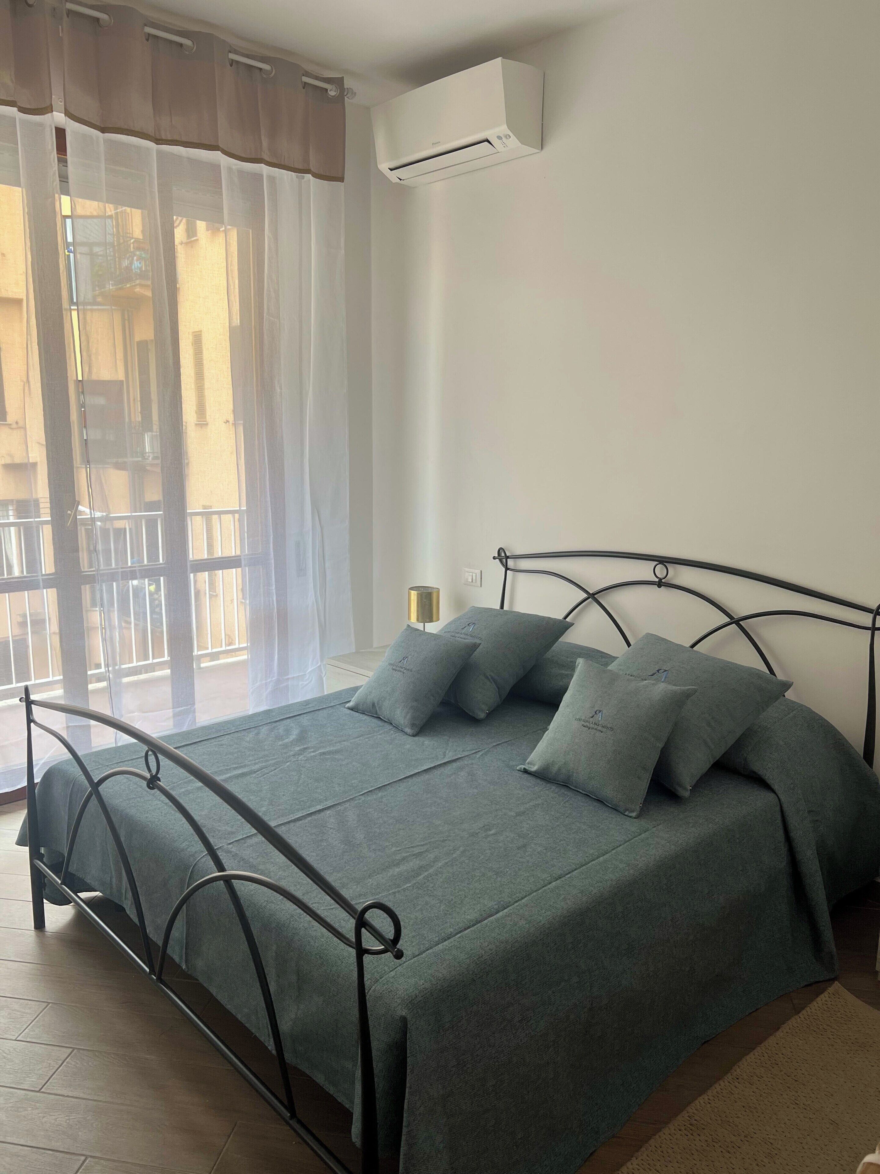 Ein Schlafzimmer mit Bett, einem Fenster mit Vorhängen, einer Klimaanlage und Blick ins Freie.