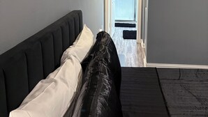A modern bedroom with a bed, a door leading to a hallway, and a wall-mounted mirror. - Welcome To Your Comfy GetAway! (Dallas)
