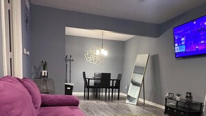 A living room with a sectional sofa, a dining table with chairs, a flat-screen TV mounted on the wall, and a ceiling fan. - Welcome To Your Comfy GetAway! (Dallas)