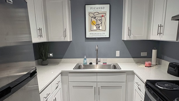 A modern kitchen with white cabinets, a stainless steel refrigerator, a sink, and a stove. - Welcome To Your Comfy GetAway! (Dallas)