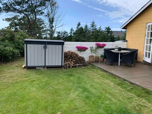 A backyard with a shed, a wooden deck, a table with chairs, and a white fence with flower boxes. - 5 Star Holiday Home in Lokken (Lokken)