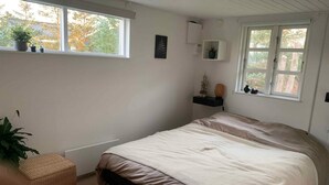 Un dormitorio con cama, ventana, una pequeña estantería con adornos y una planta en maceta.