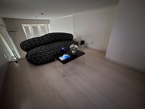 Un salon moderne avec un canapé noir à motifs, une table basse sur laquelle se trouve un objet bleu, et une porte blanche en arrière-plan.