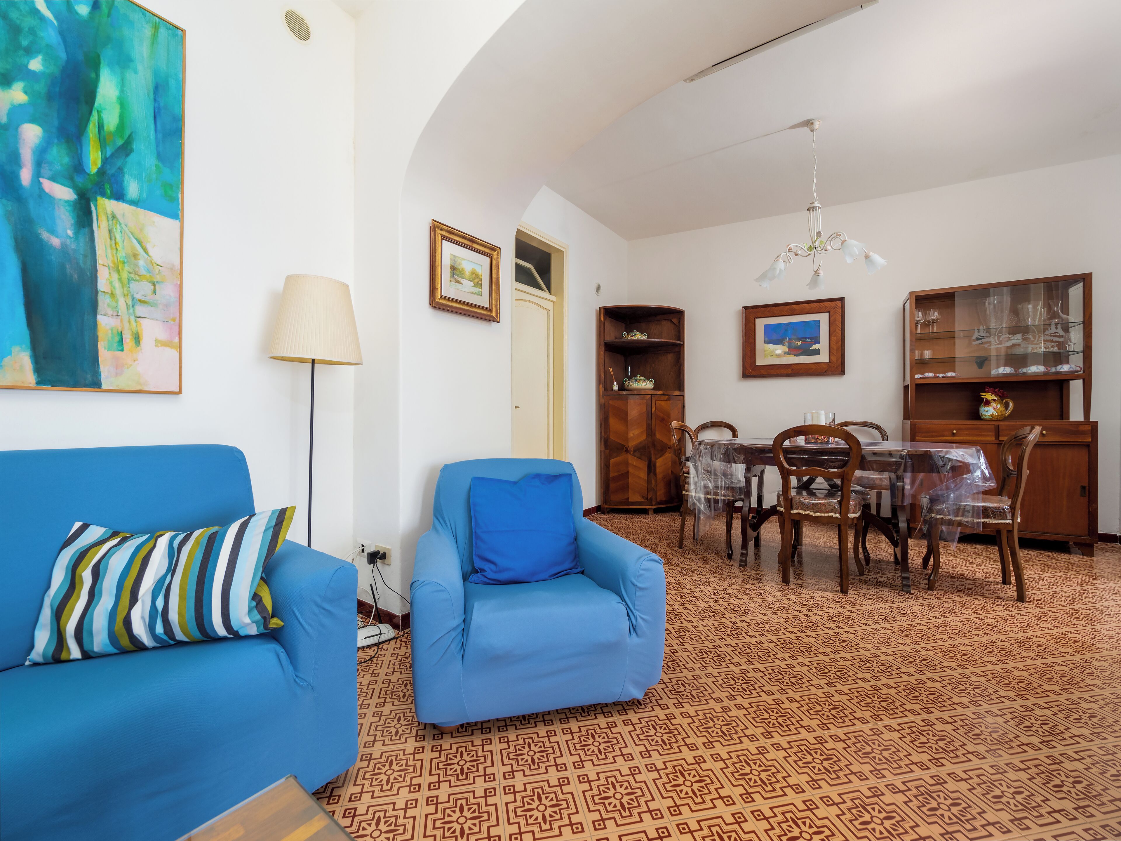 Una sala de estar con un sofá azul, una mesa de comedor con sillas, un mueble de madera y un piso con diseño.