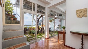A staircase with patterned steps leading to a glass door, a wooden table, and a view of a garden and outdoor area. - Scorcio d'Oltremare (Positano)