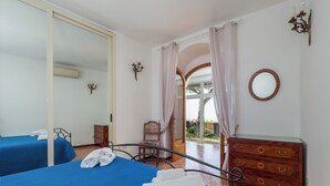 A hotel room with two beds, a wooden dresser, a mirror, and a view of the outside. - Scorcio d'Oltremare (Positano)