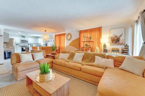 Ein modernes Wohnzimmer mit einer Sofagarnitur, einem Couchtisch und einer Küche im Hintergrund.