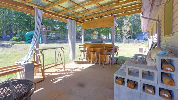 An outdoor patio with a wooden pergola, a barbecue area, and a play structure in the background. - Playground & Grill: Pet-Friendly Griffin Getaway! (Griffin)