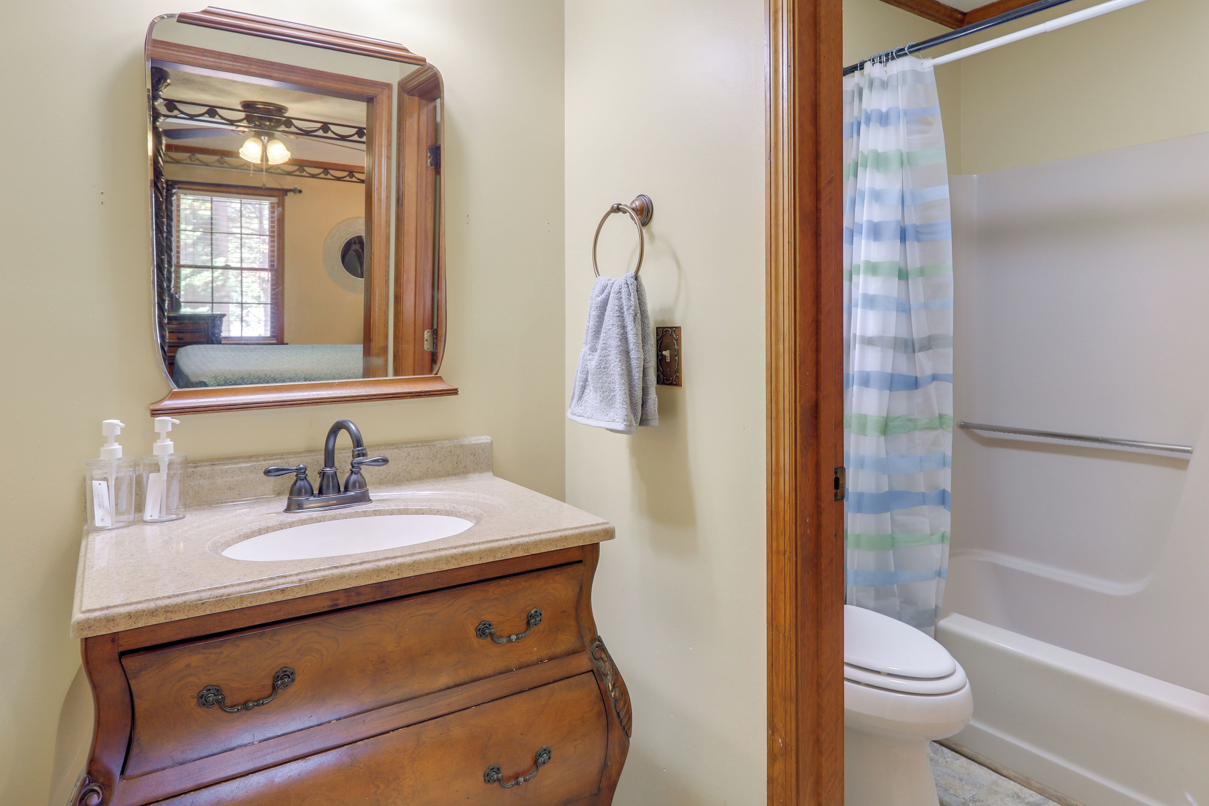 A bathroom with a wooden vanity, a sink, a mirror, a towel ring, and a shower with a striped curtain.
