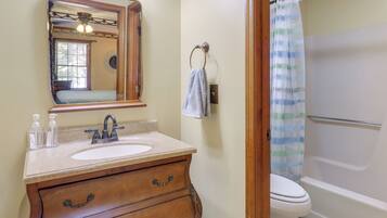 A bathroom with a wooden vanity, a sink, a mirror, a towel ring, and a shower with a striped curtain.