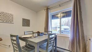 Uma sala de jantar com mesa e cadeiras, uma janela com cortinas e arte decorativa na parede.