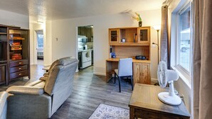 Um espaço compacto com sofá, escrivaninha, cadeira, ventilador e janela com cortinas.