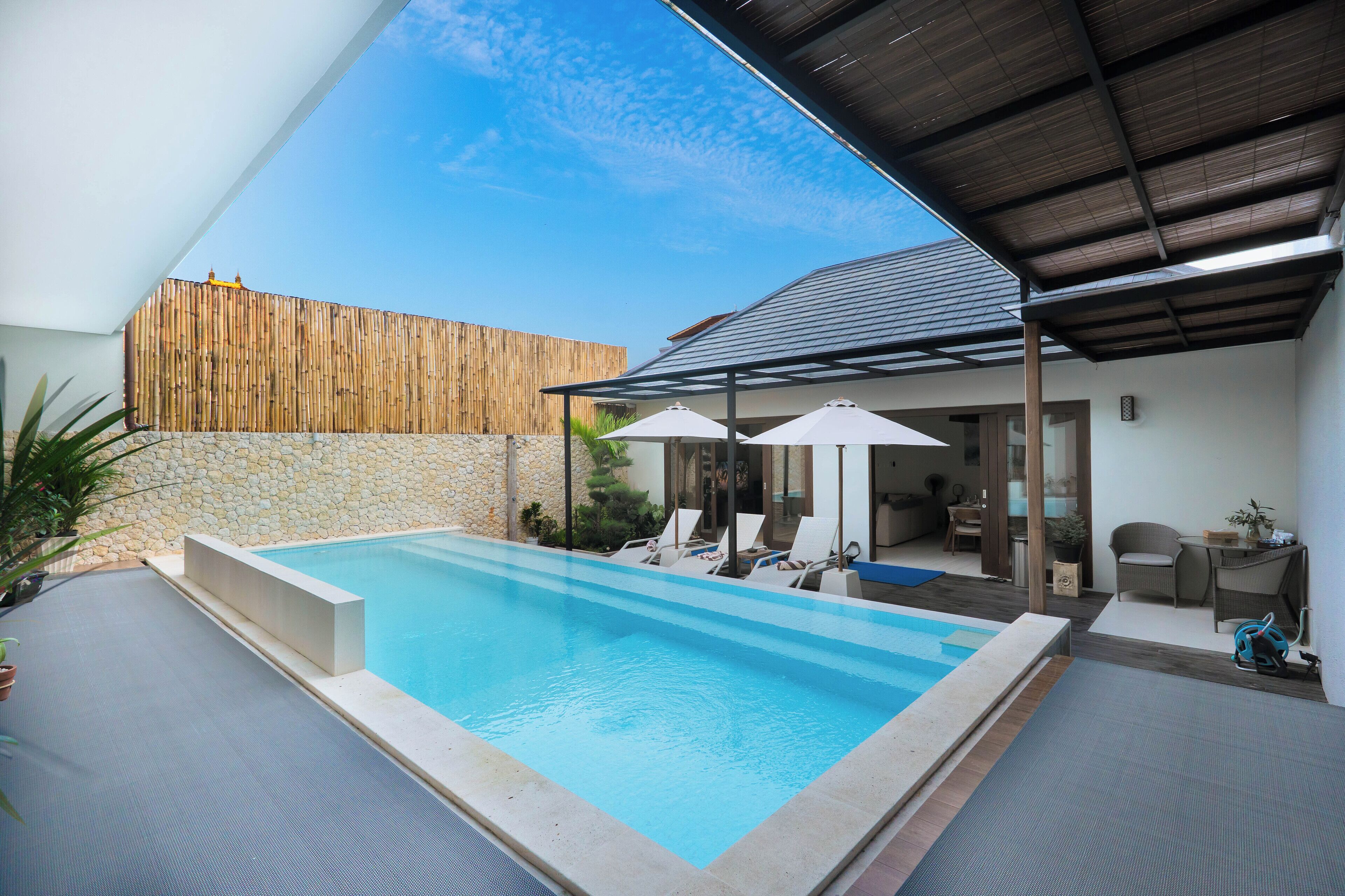Une piscine avec des chaises longues et des parasols, un patio couvert et un mur en pierre.