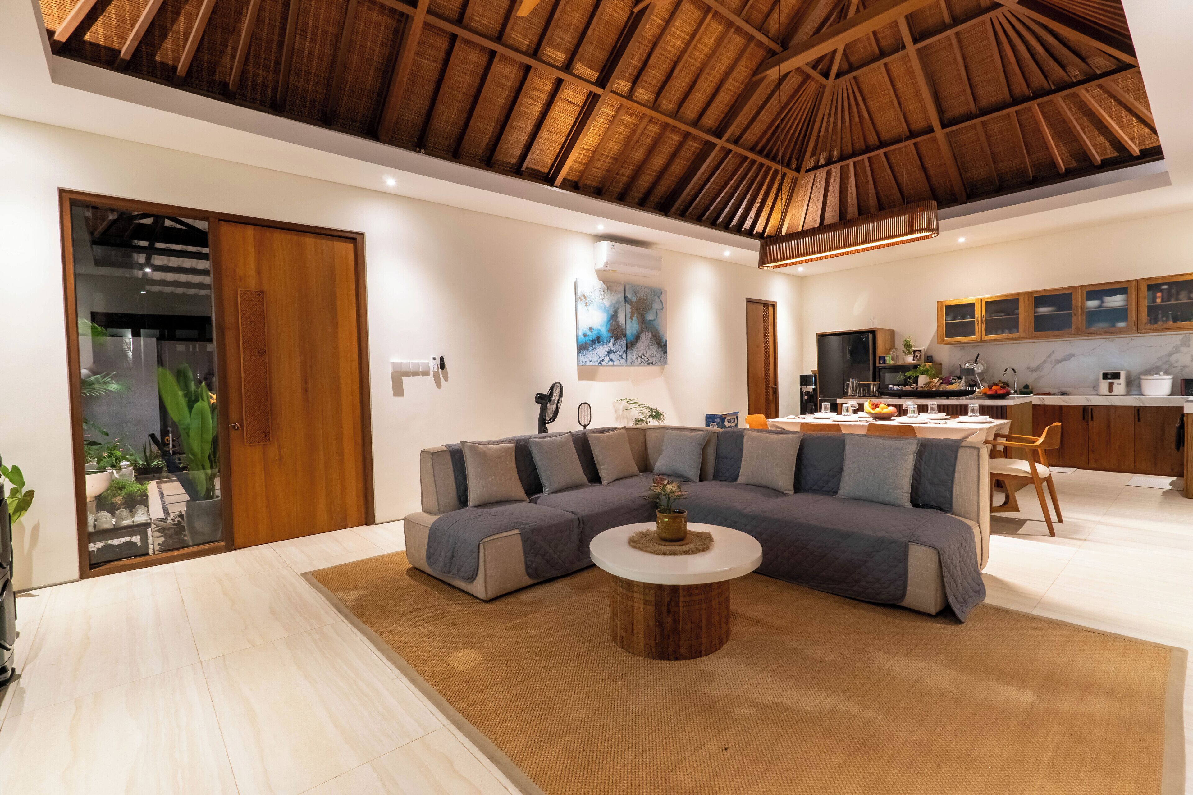 Een moderne woonkamer met een hoekbank, een ronde salontafel en een keukenhoek met houten kasten en een eettafel.