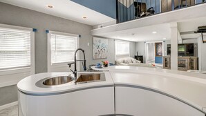 Una cocina moderna con una isla central, un comedor con mesa redonda y una sala de estar con sofá y televisor.