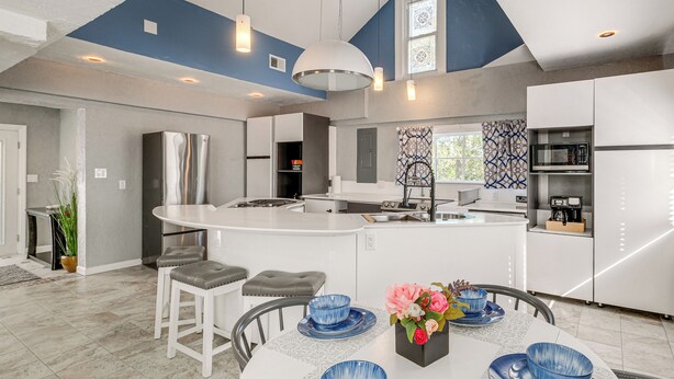 Una cocina moderna con una isla central, muebles blancos y una pared de acento azul.