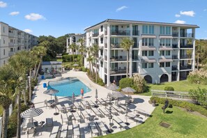 A hotel with a swimming pool, outdoor seating, and a multi-story building with balconies.