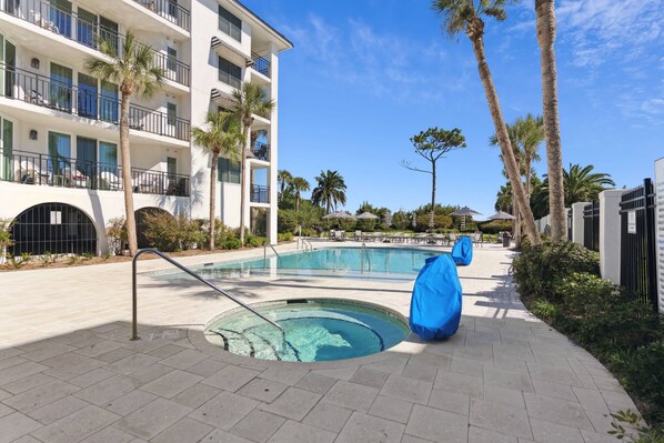 A hotel with a swimming pool, palm trees, and a covered seating area.