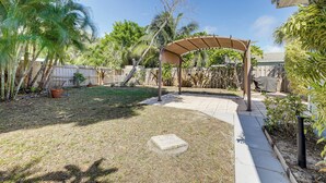 A backyard with a covered patio area, a concrete slab, and various plants. - 3 Mi to Jensen Beach: Pet-Friendly Getaway w/ Yard (Jensen Beach)