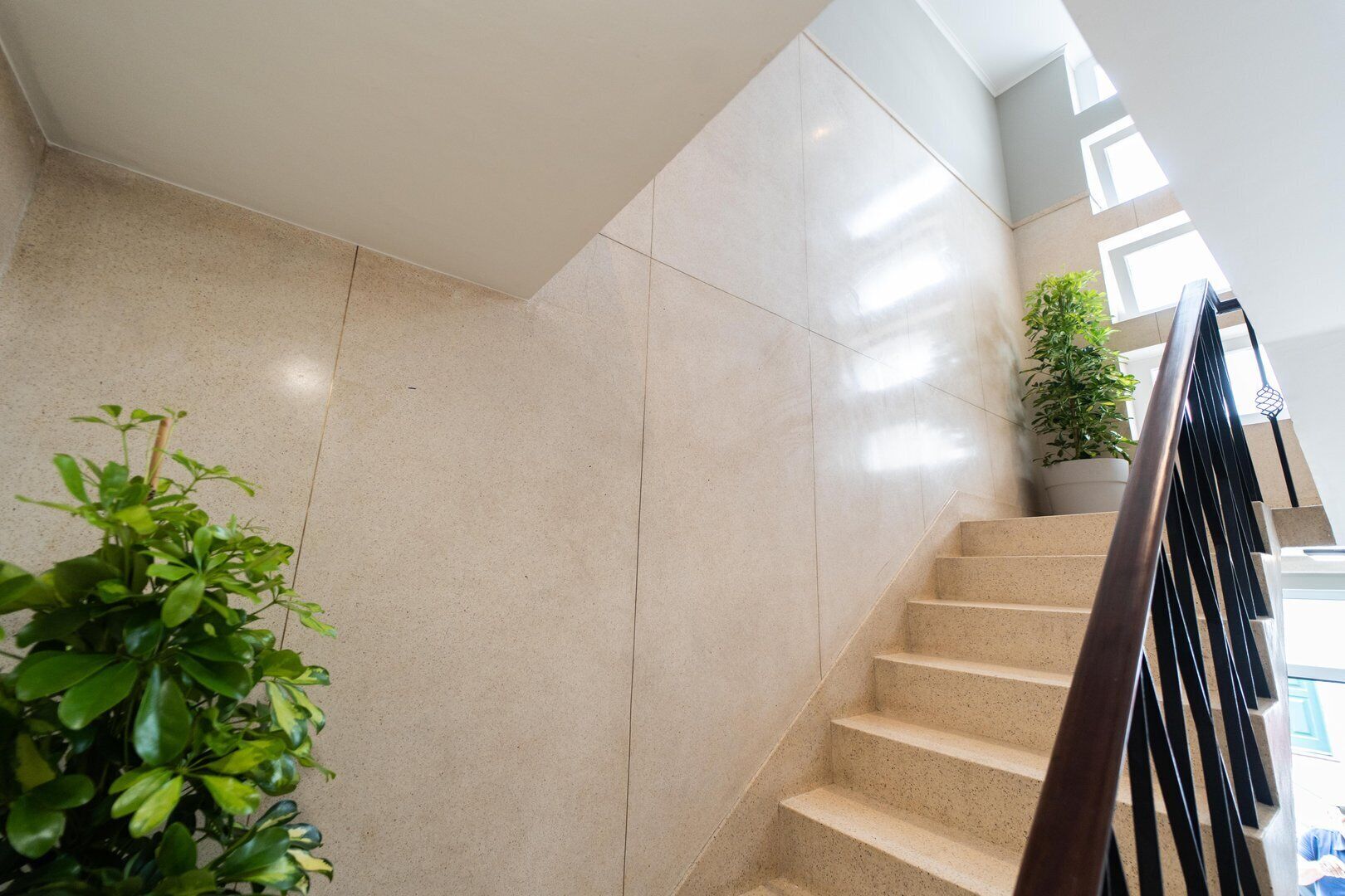 A modern staircase with beige tiles, a metal railing, and a potted plant on the landing.