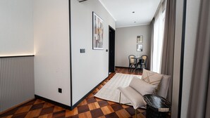 Une chambre d’hôtel moderne avec un parquet à carreaux, un canapé, une petite table et une vue sur la salle à manger.