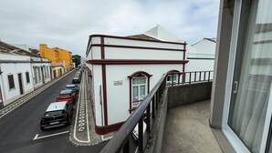 Une vue de rue avec un immeuble dont la façade est blanche et les bordures rouges. Des voitures sont garées le long de la rue, et une enseigne sur l’immeuble indique « JOSE BENSAIDE ».