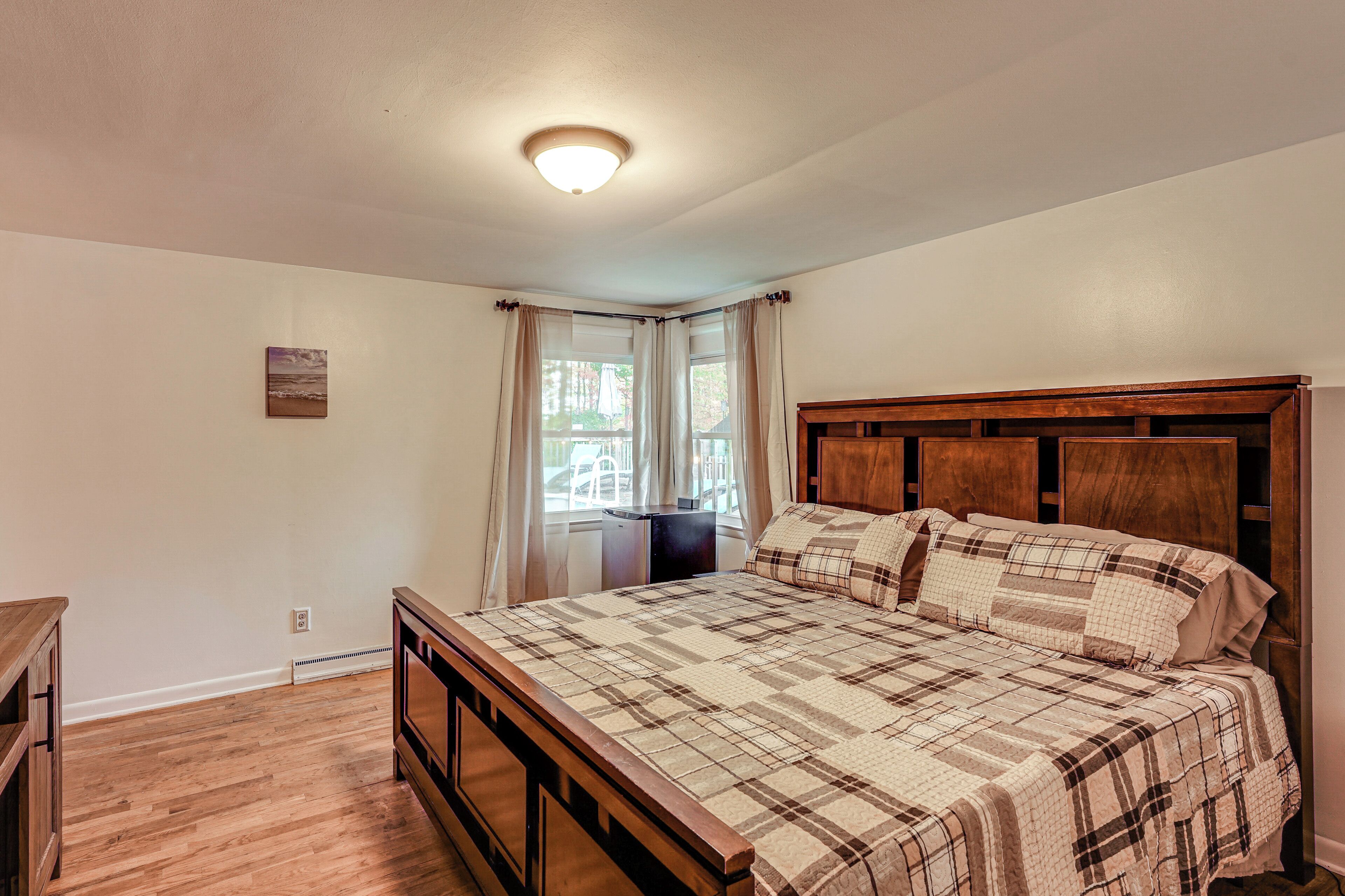 A bedroom with a wooden bed, a nightstand, a window with curtains, and a ceiling light.