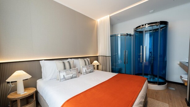 Une chambre d’hôtel moderne dotée d’un grand lit, d’une table de chevet avec une lampe, d’une douche en verre et d’un petit coin salon.