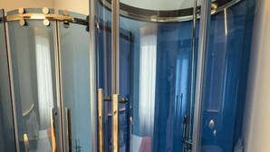 Une pièce comprenant une cabine de douche circulaire fermée par des parois de verre, des toilettes et un lavabo.