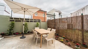 Une terrasse avec une table et des chaises, entourée d’une clôture en bambou, et protégée par un grand parasol.
