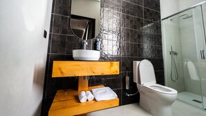 Ein Badezimmer mit weißem Waschbecken, einem Spiegel, einem Holzschrank, einer Toilette und einer Duschkabine aus Glas.