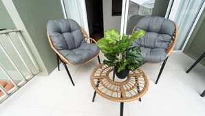 Ein Balkon mit zwei Korbstühlen, einem runden Tisch und einem Blumentopf.