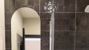 Un bagno moderno con un lavandino tondo, un mobile contenitore in legno, uno specchio grande e un box doccia in vetro.