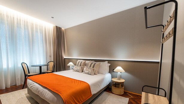 Una camera d'albergo con un letto grande, un tavolino, una sedia, una lampada e una televisione.