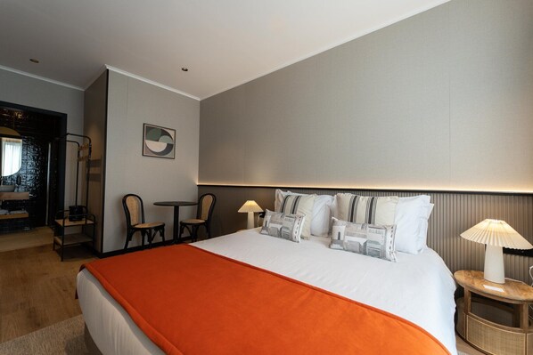 Une chambre d’hôtel avec un grand lit, deux chaises, une petite table et une lampe.