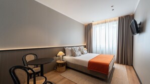 Habitación de hotel con cama, escritorio, silla, televisor y ventana con cortinas.