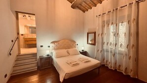 A bedroom with a bed, bedside tables, a mirror, and a window with curtains. - City / Village Apartment in Cortona with 2 bedrooms sleeps 4 (Cortona)