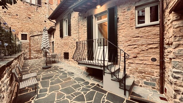 A stone building with a stone-paved patio, outdoor seating, and a metal railing. - City / Village Apartment in Cortona with 2 bedrooms sleeps 4 (Cortona)
