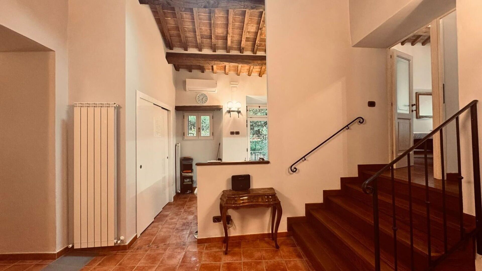 A staircase with a wooden handrail and a tiled floor leading to a landing with a small table and a clock.
