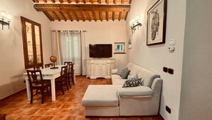 A living room with a white sofa, a dining table with chairs, a TV on a white cabinet, and a globe on the table. - City / Village Apartment in Cortona with 2 bedrooms sleeps 4 (Cortona)
