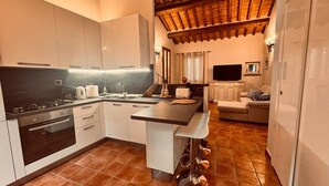 A modern kitchen with a central island, a dining area with a sofa, and a TV mounted on the wall. - City / Village Apartment in Cortona with 2 bedrooms sleeps 4 (Cortona)