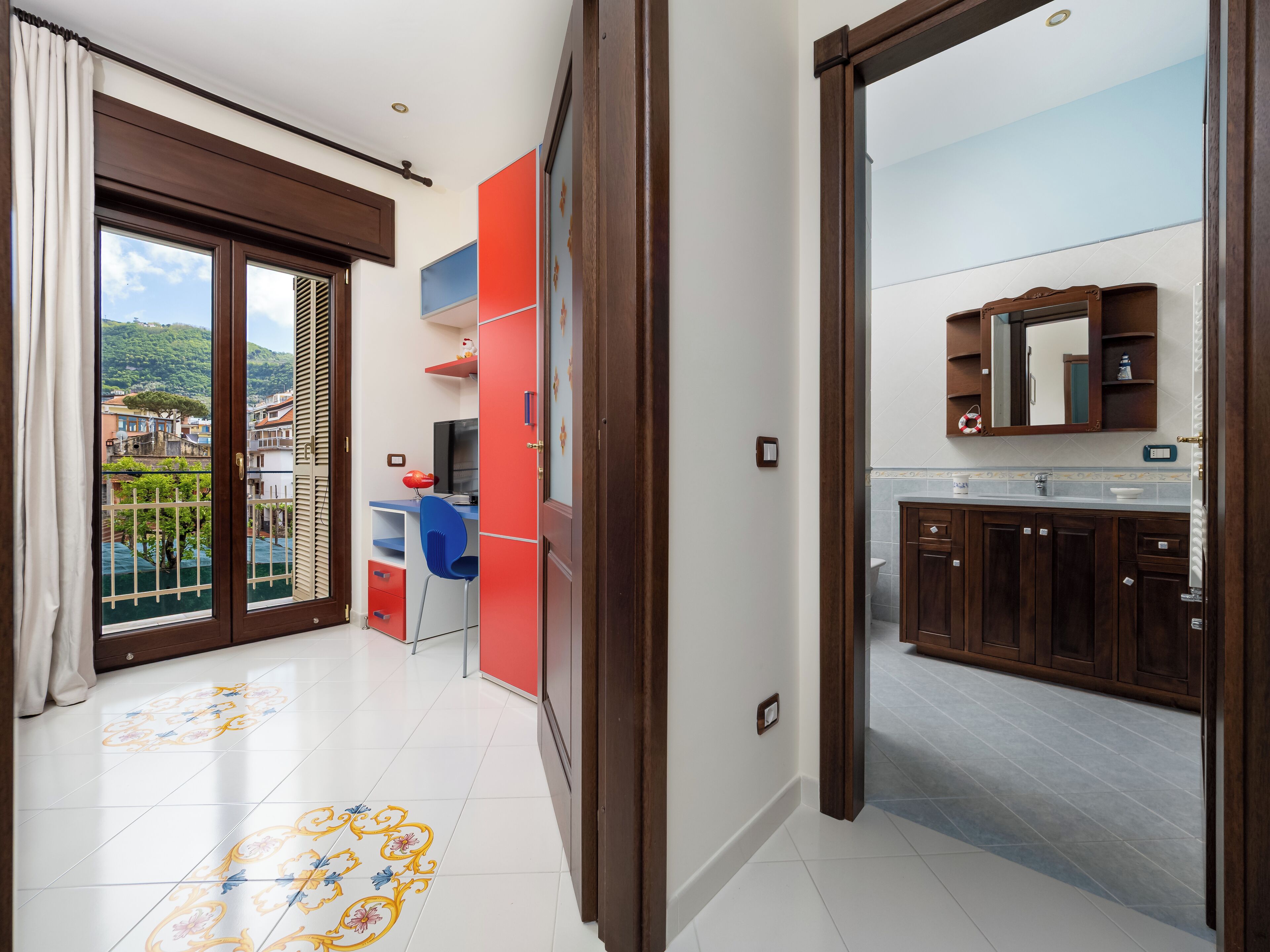 A spacious room with a balcony, a modern bathroom, and a view of a hillside.