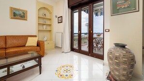 A living room with a brown leather sofa, a glass coffee table, a white radiator, a large vase, and a view of the sea through a glass door. - Residenza Le Sirene (Sorrento)